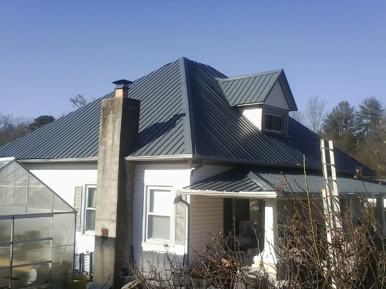 Dark blue standing seam metal roof on a white farmhouse with dormer — Slate & Tile Roof Repair by Roofing Brothers in Cunningham