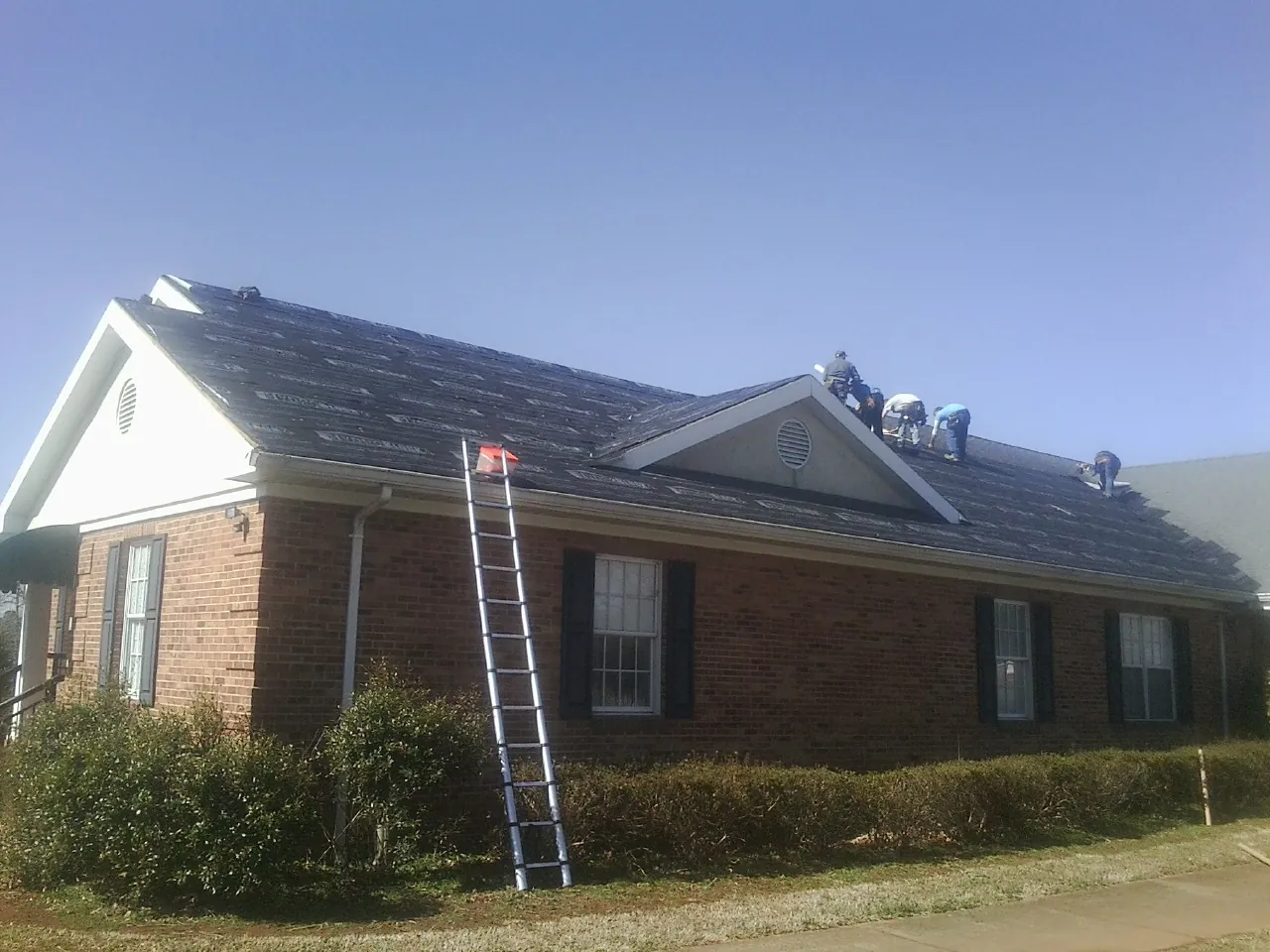 Crew tearing shingles off a brick ranch roof with a ladder set — Metal Roof Repair work by our crew in Cunningham