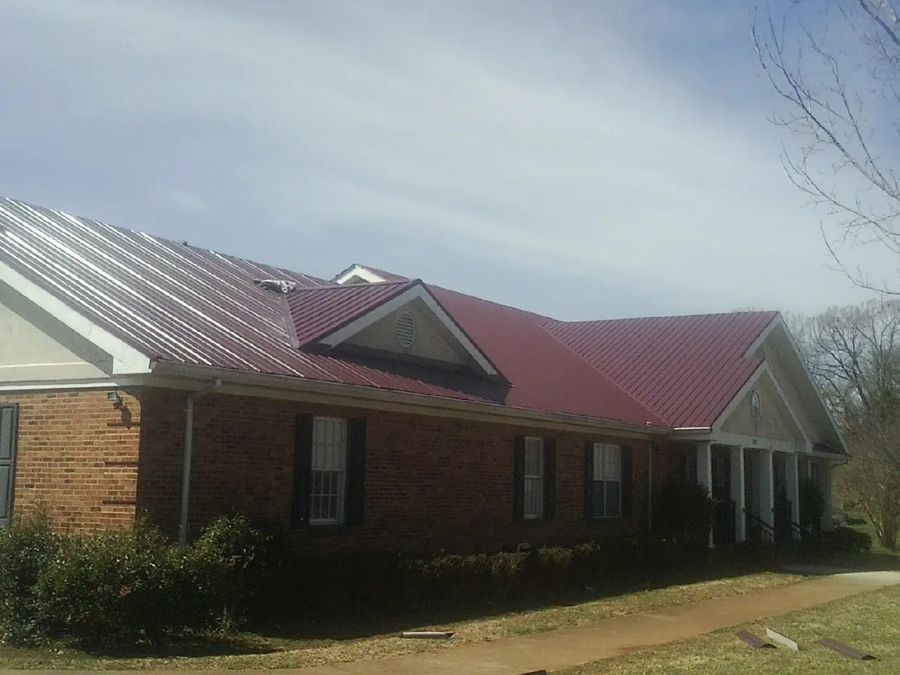 Red metal roof with gabled entries on a long brick building, from a Hail Damage Roof Repair job in Cunningham