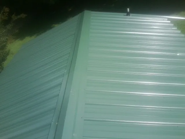 New green metal panels meeting at the ridge of a roof — Flat Roof Repair work by our crew in Cunningham
