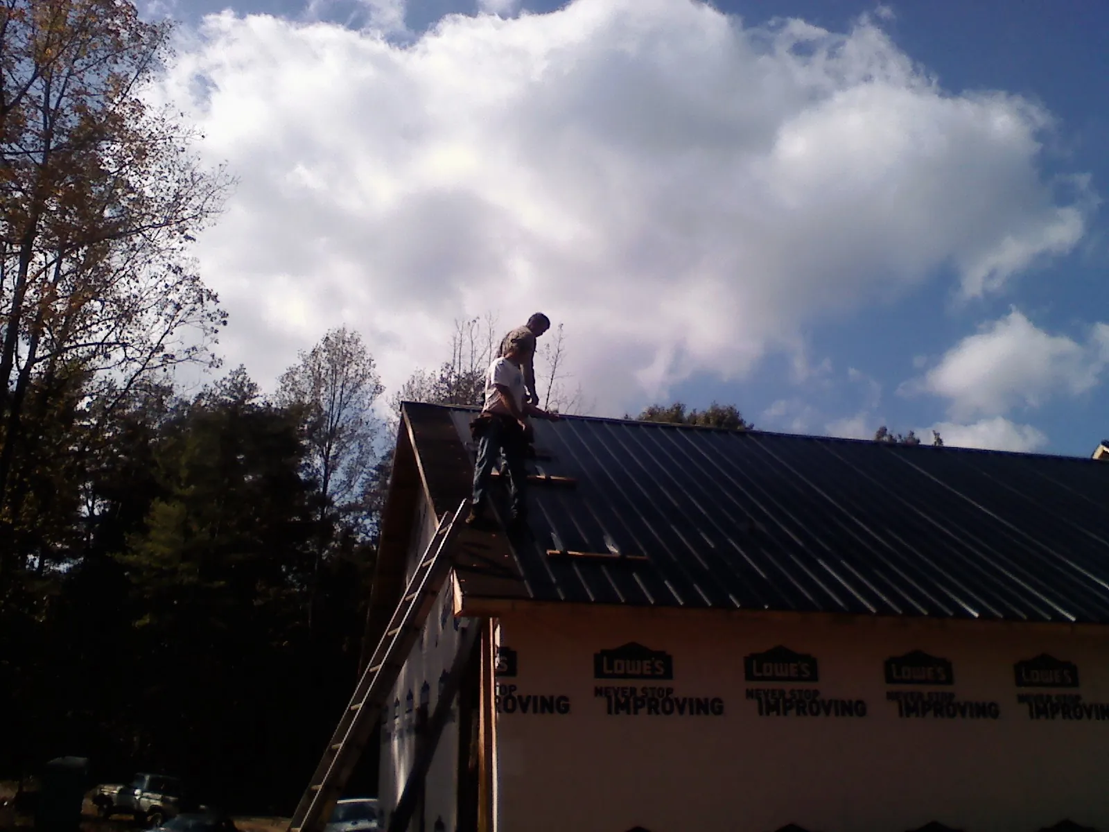 Roofer fastening dark metal panels high against a cloudy sky, from a Roof Inspection job in Cunningham