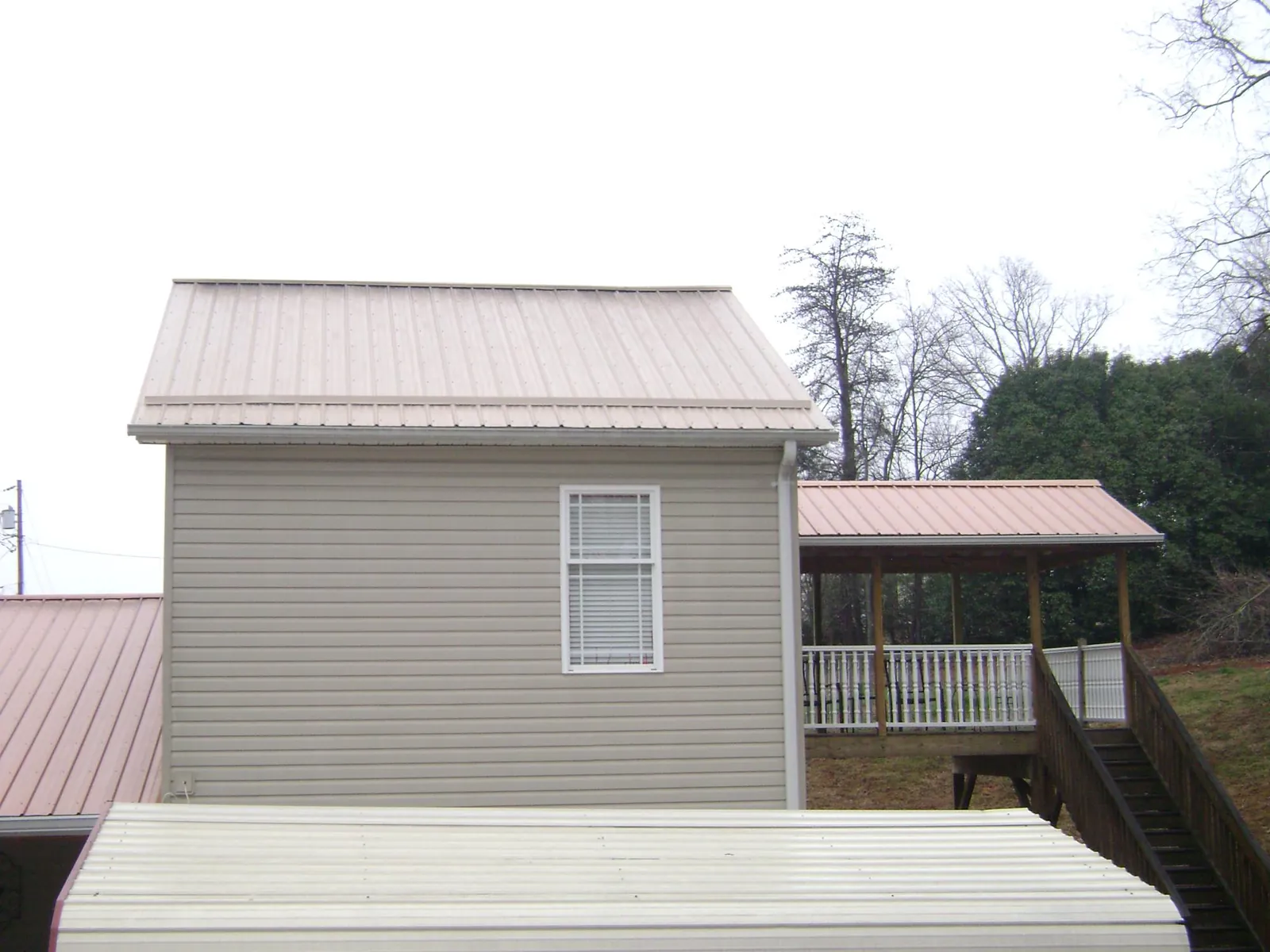 Tan metal roofs on a two story addition and attached porch, from a Roof Replacement job in Cunningham